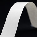 Cinta de tela blanca curvada sobre fondo negro, mostrando textura y grosor.